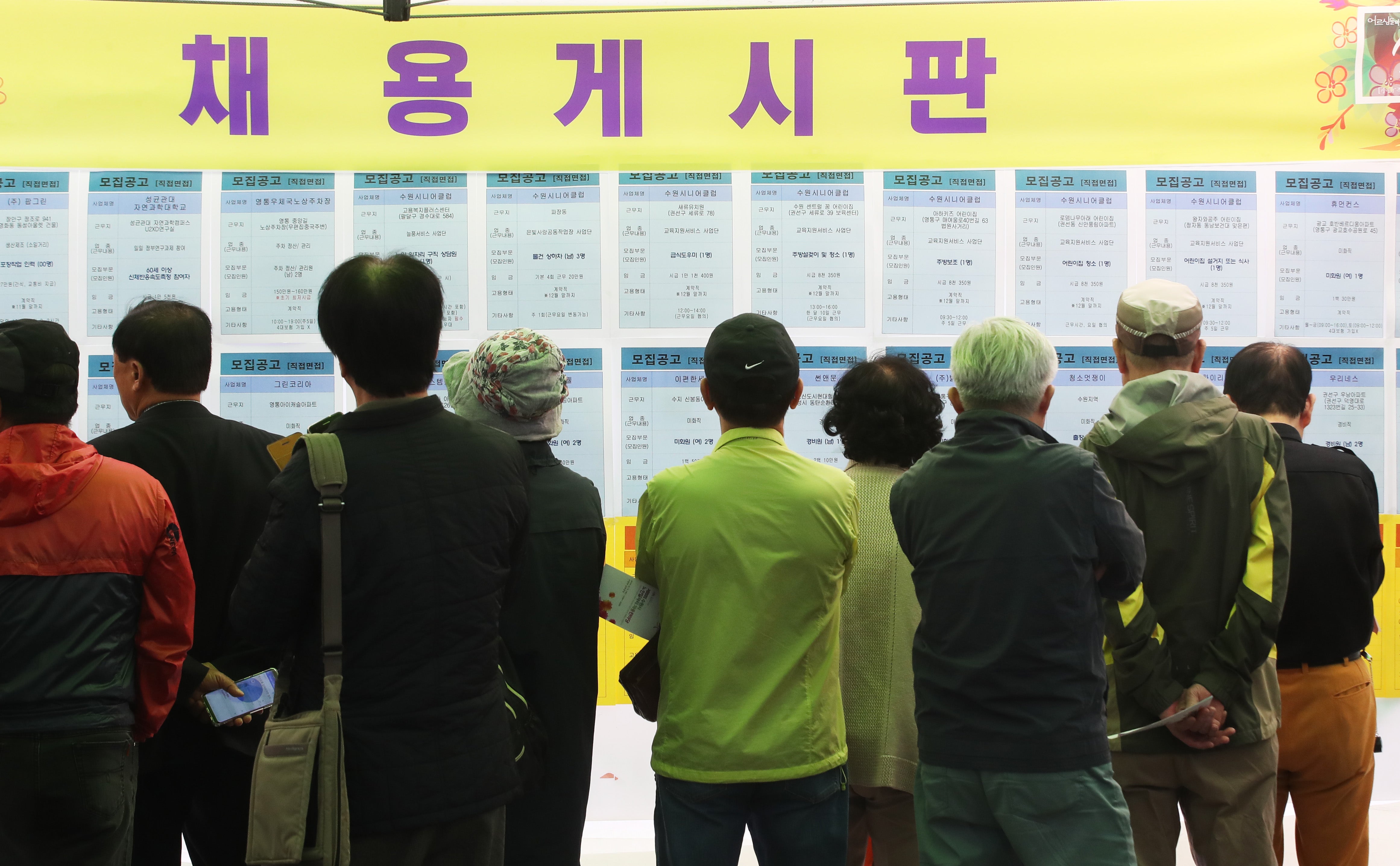 Older people look at a recruitment bulletin board at a job fair