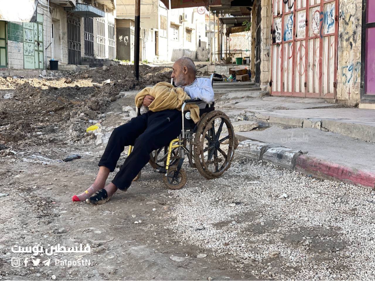 An older man sits in a wheelchair on a bulldozed street