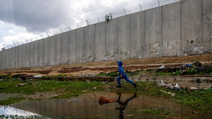 A boy runs alongside a tall concrete wall