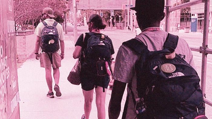 People wearing backpacks walking on city sidewalk