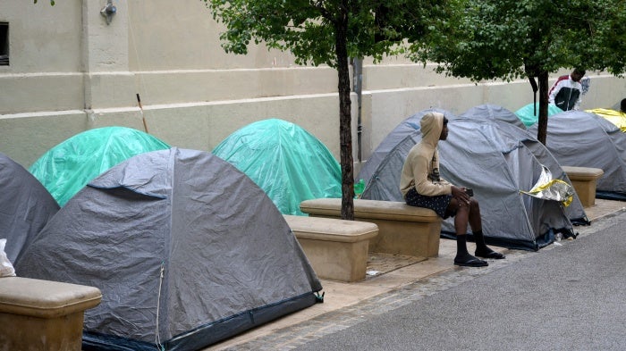 An unaccompanied migrant child sits on a bench at an encampment