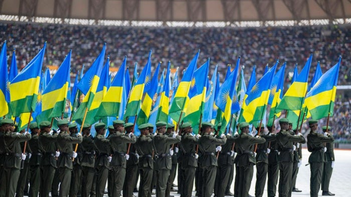 Members of the Rwanda Defence Forces march while holding Rwanda flags in a stadium