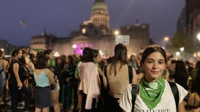 A woman wearing a t-shirt that says "Feminist" on it poses amidst a rally