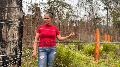 A woman stands in the forest with her hand on a wire fence.