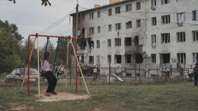 A girl on a swing looks at an apartment building in the Industrialnyi district of Kharkiv, Ukraine, damaged by a Russian drone attack that killed 7 people (including children) and injured 23, on August 18, 2025.