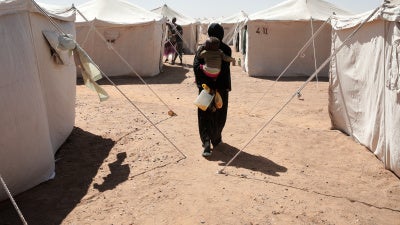 A Sudanese woman displaced from El-Fasher carries her child as she walks between tents at El-Afadh camp in Al Dabbah, in Sudan's Northern State, November 16, 2025. 