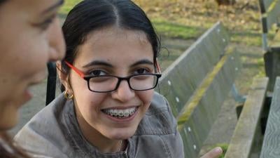 close up of Nujeen Mustafa, a young Syrian disability rights advocate, sitting on a park bench smiling