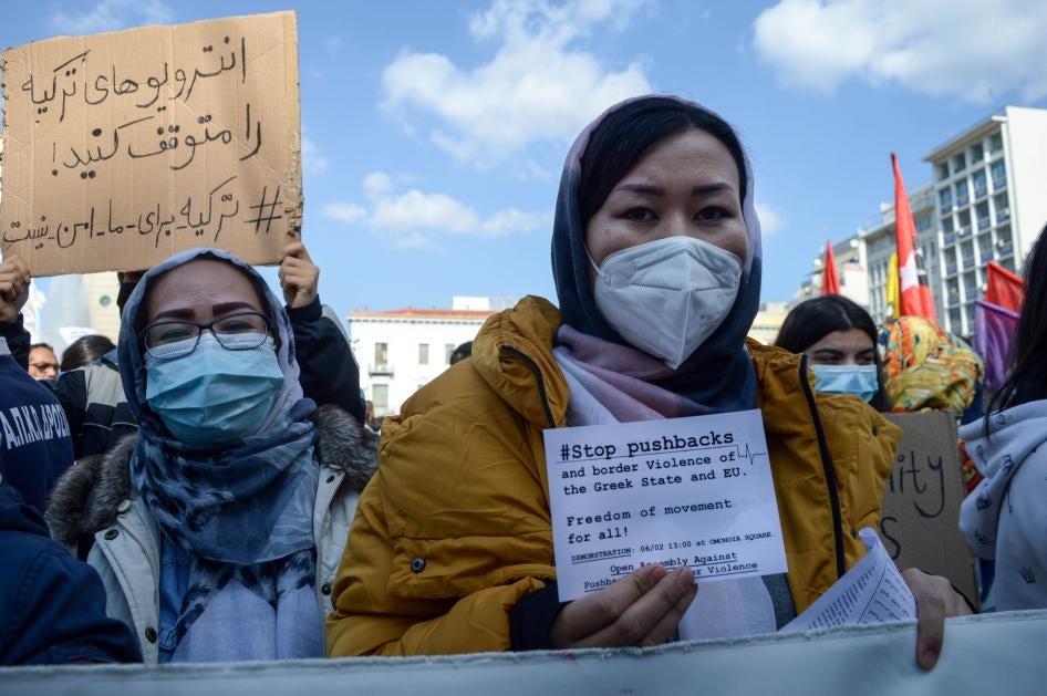 A woman at a protest holds a sign that reads "#StopPushbacks"