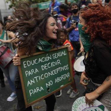 Two women jump and smile while holding a protest sign