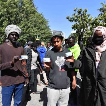 Sudanese and Yemeni men show their refugee or asylum seeker cards on April 12, 2023 outside the International Organization for Migration (IOM) office in Tunis, after Tunisian police on April 11 used force and tear gas to disperse refugees, asylum seekers, and migrants and dismantled their makeshift camp in front of the nearby UN Refugee Agency (UNHCR) office in Tunis. © 2023 Fethi Belaid/AFP via Getty Images