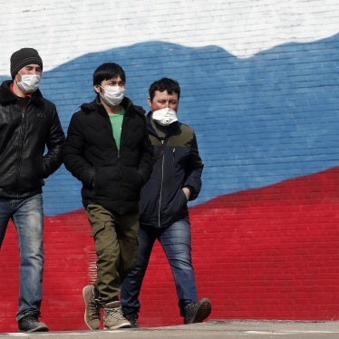 Three men in face masks walk in front of a mural of the Russian flag