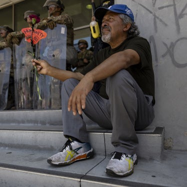A man holds a flower and the message "Humanity for All" in front of a line of soldiers