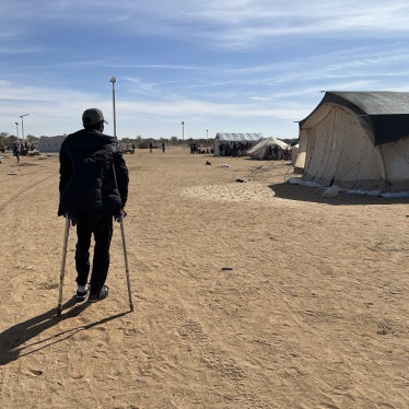 A man stands on crutches in a refugee camp