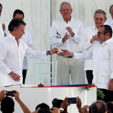 Colombian President Juan Manuel Santos hands a lapel pin in shape of a dove to Timochenko after signing a peace accord.