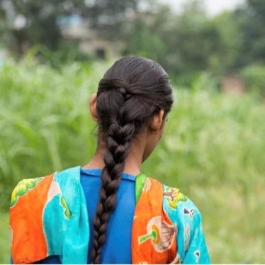 A young girl with long hair portraid from behind, in front of a field. 